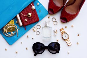 Fashionable female accessories watch sunglasses lipstick blue clutch and red shoes . Overhead of essentials for stylish young woman.